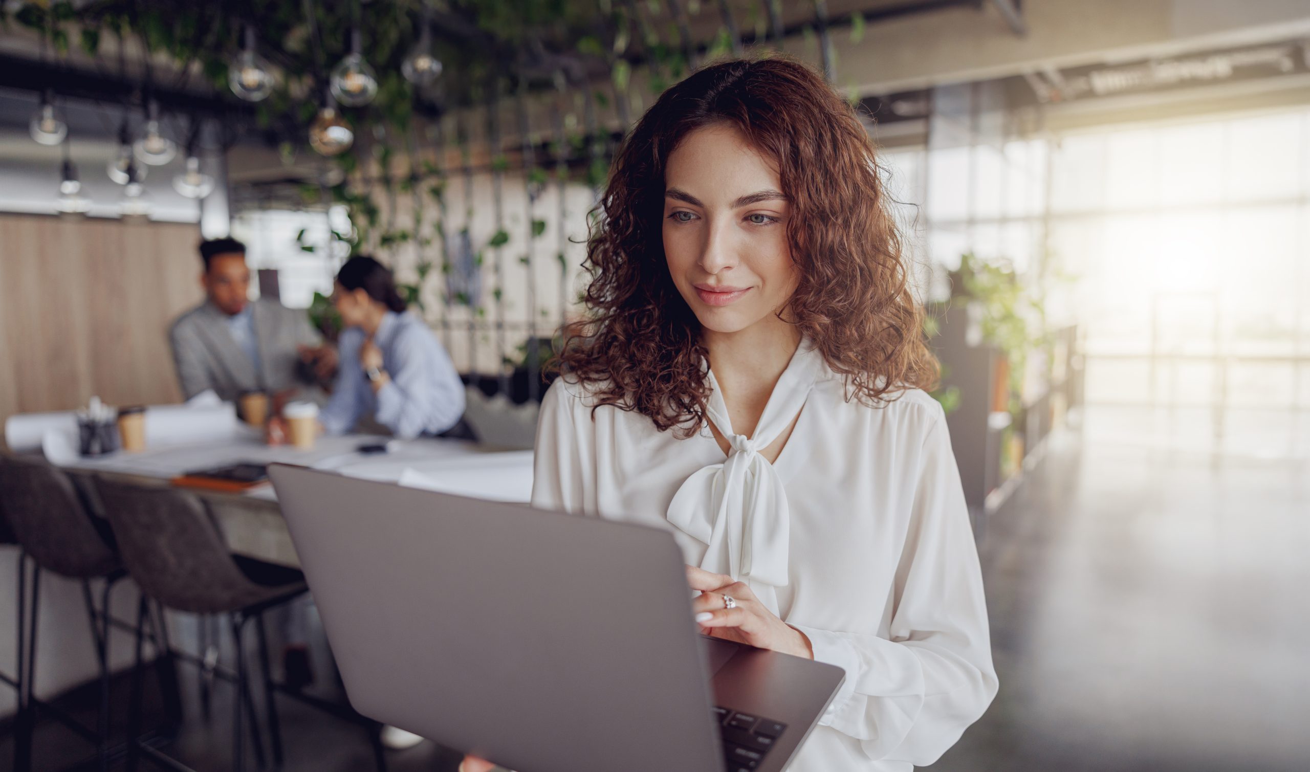 A woman intently using her laptop in a stylish office, collaborating effectively with her colleagues